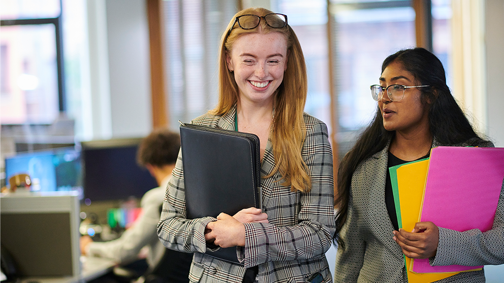 two young professionals walking side by side in a workplace.