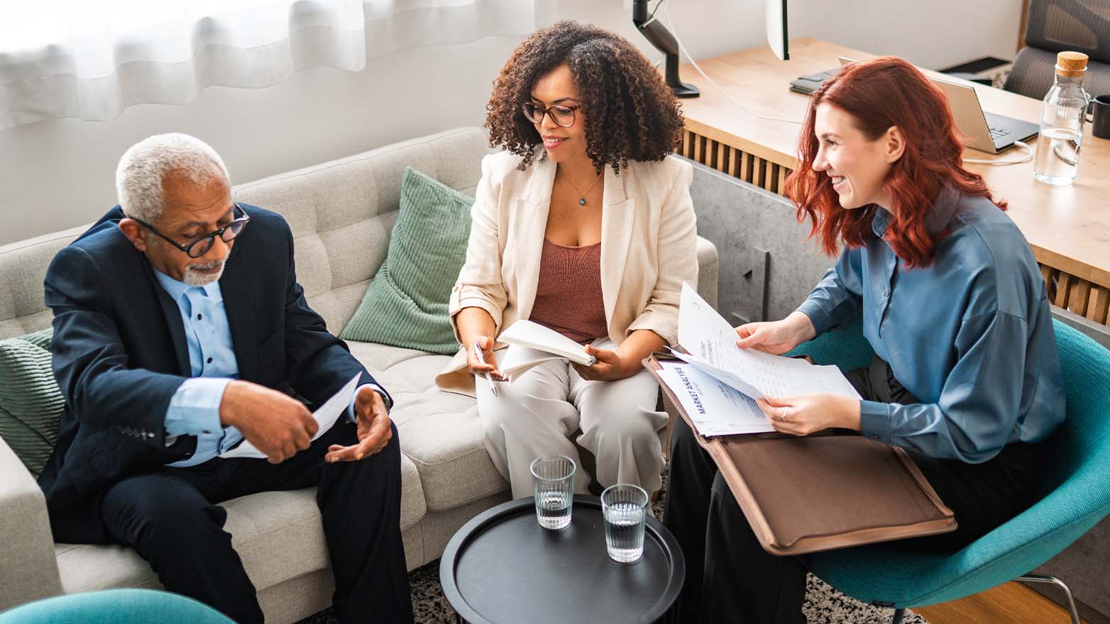 Three people meet in a comfortable office setting to review financial documents and discuss goals while evaluating financial planning and advisory options.
