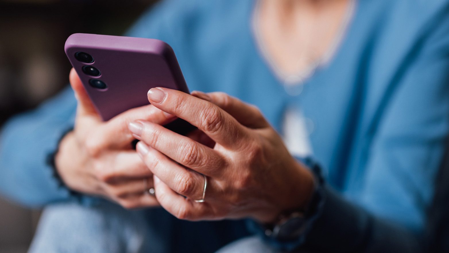 Close-up of a person holding and using a smartphone with both hands, with the device in focus and the background softly blurred.