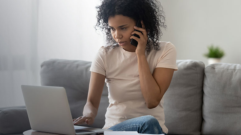 Young woman talking on phone with laptop sitting on a couch.