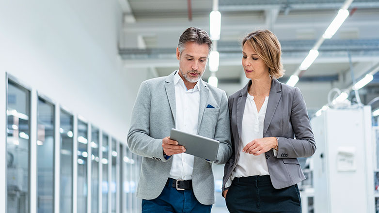 Male and female business owner looking at a tablet in the middle of their warehouse.