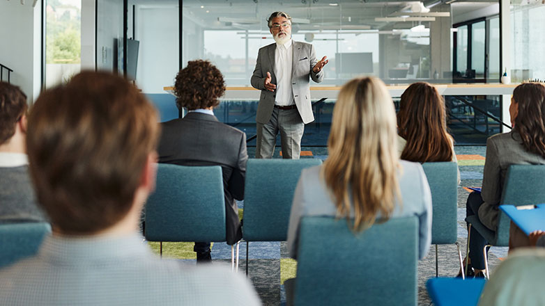 Business presentation with a speaker standing at the head of the room.