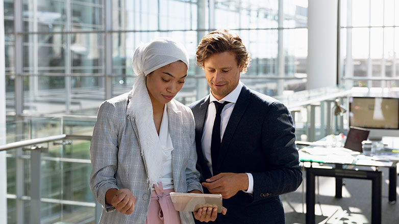 Male and female coworker in an office looking at a tablet.