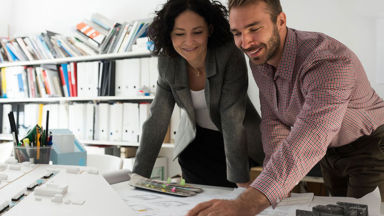 Two work colleagues review papers together on a work desk.