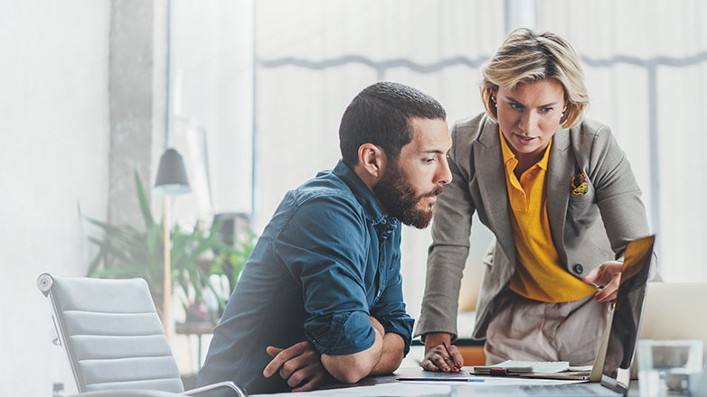 Male and female co-workers in a conference room looking at laptop.