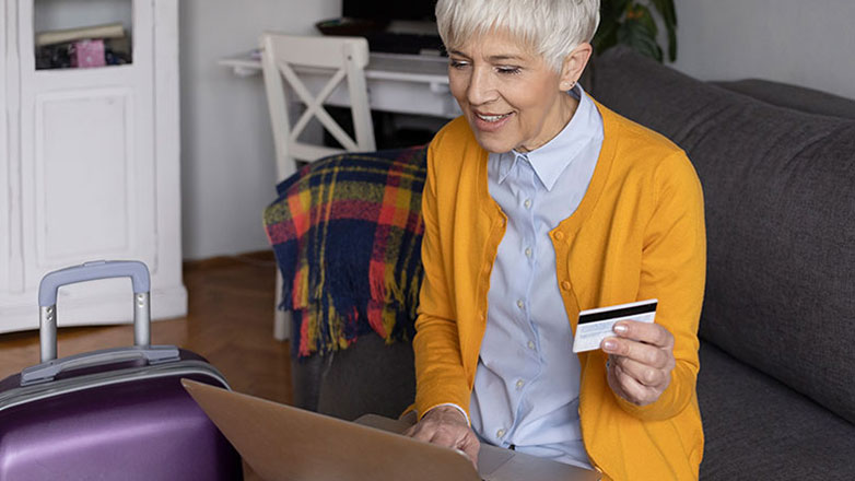 Elderly woman books a flight online using her credit card.