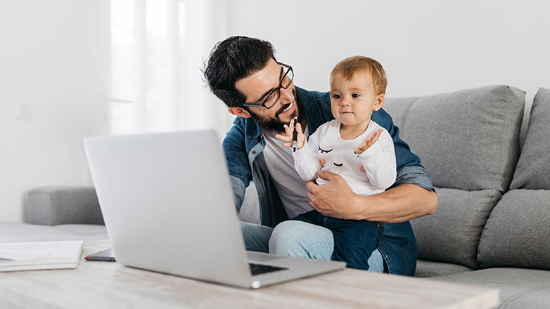 Father and baby daughter sitting on the couch working on laptop.