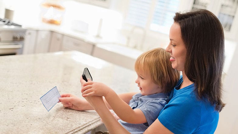 Mom deposits her check with mobile phone while holding baby.