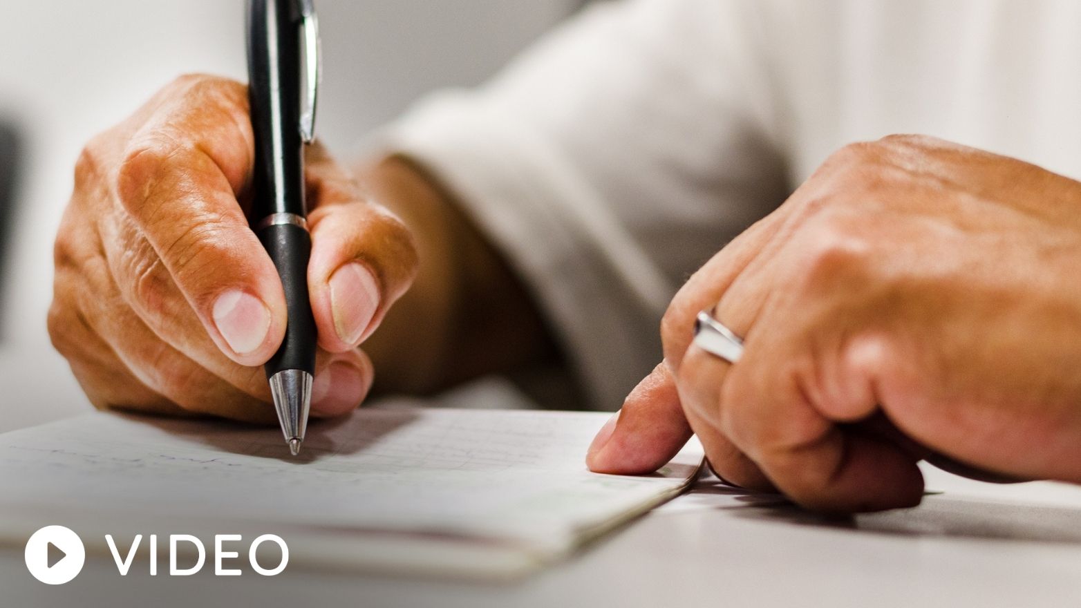 Close-up of hands writing on a check with a black pen.