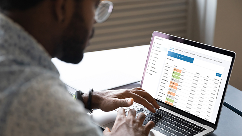 A person is using a laptop computer. He is looking at a screen with a table of data. He is wearing glasses and has a watch on his left hand.