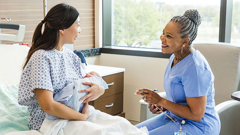 Nurse happily checks in with a new mother at her bedside in the hospital.