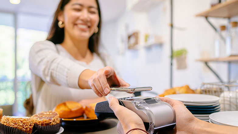 Woman uses smartphone to pay for her goods from a bakery.