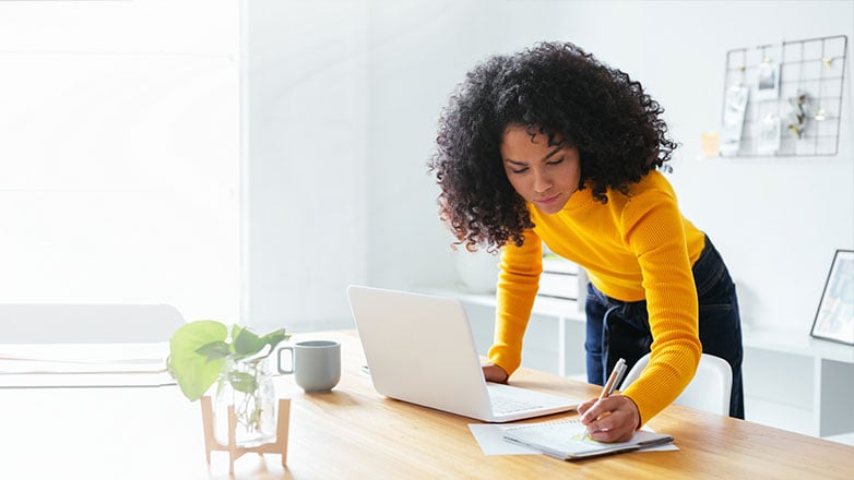 Woman standing at her desk writing in a notepad.