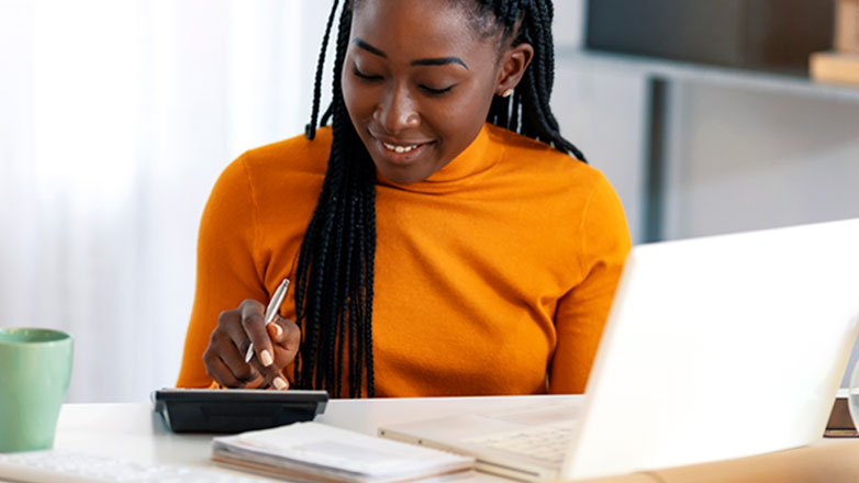 Woman uses a calculator while doing accounting work on her work laptop.