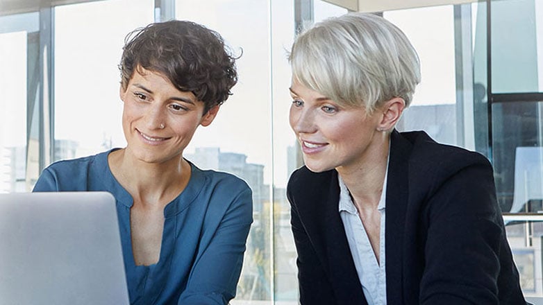 Female colleagues sit at a desk together and work on a laptop.