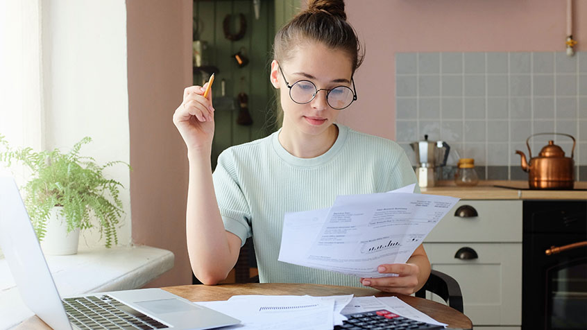 Young woman looking over paperwork using her laptop