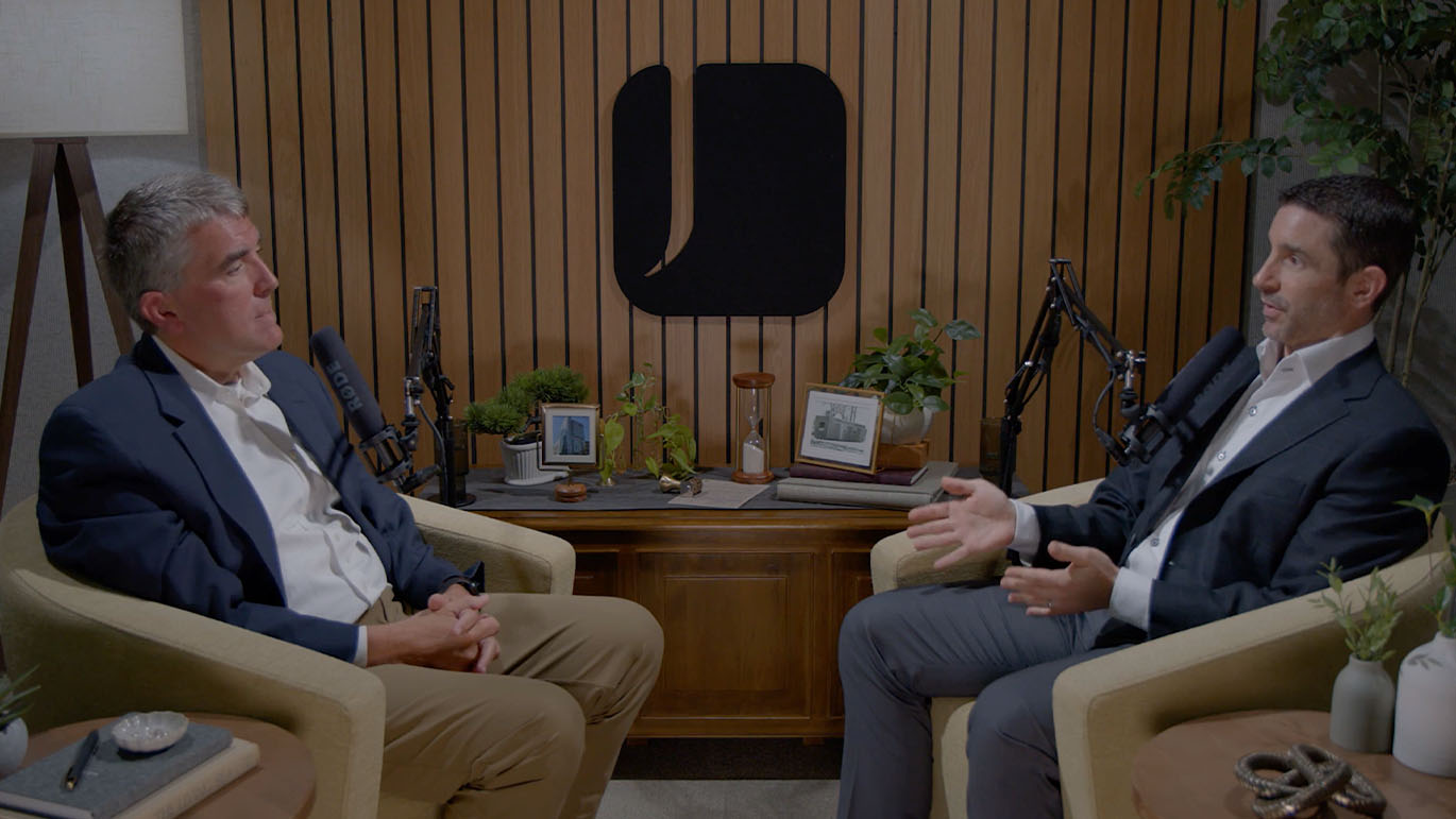 Behind-the-scenes view of a The Trusted Room podcast episode, showing two speakers engaged in a studio discussion with professional microphones.