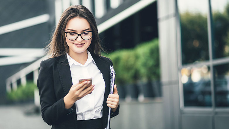 business woman looking at phone smiling walking down sidewalk