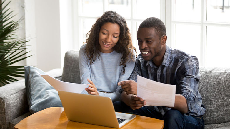 couple doing paperwork on couch in front of laptop