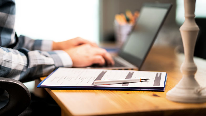 Person sitting at desk working on computer and paperwork