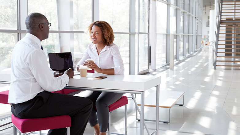 woman and man sitting at table with laptop by windows