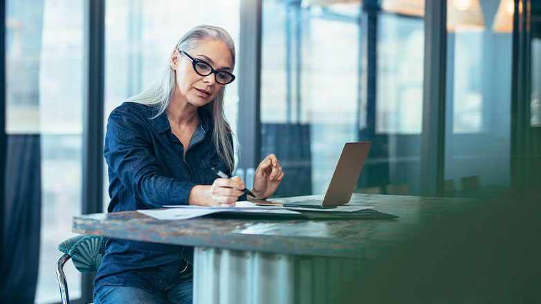 woman doing paperwork at desk with laptop