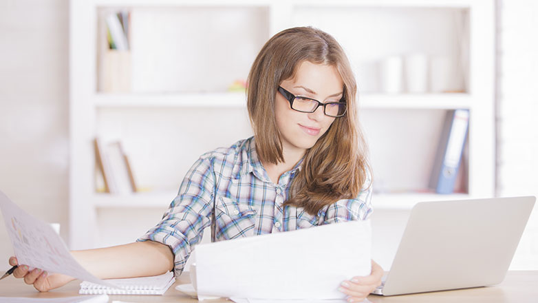 Woman sitting alone at her computer with paperwork.