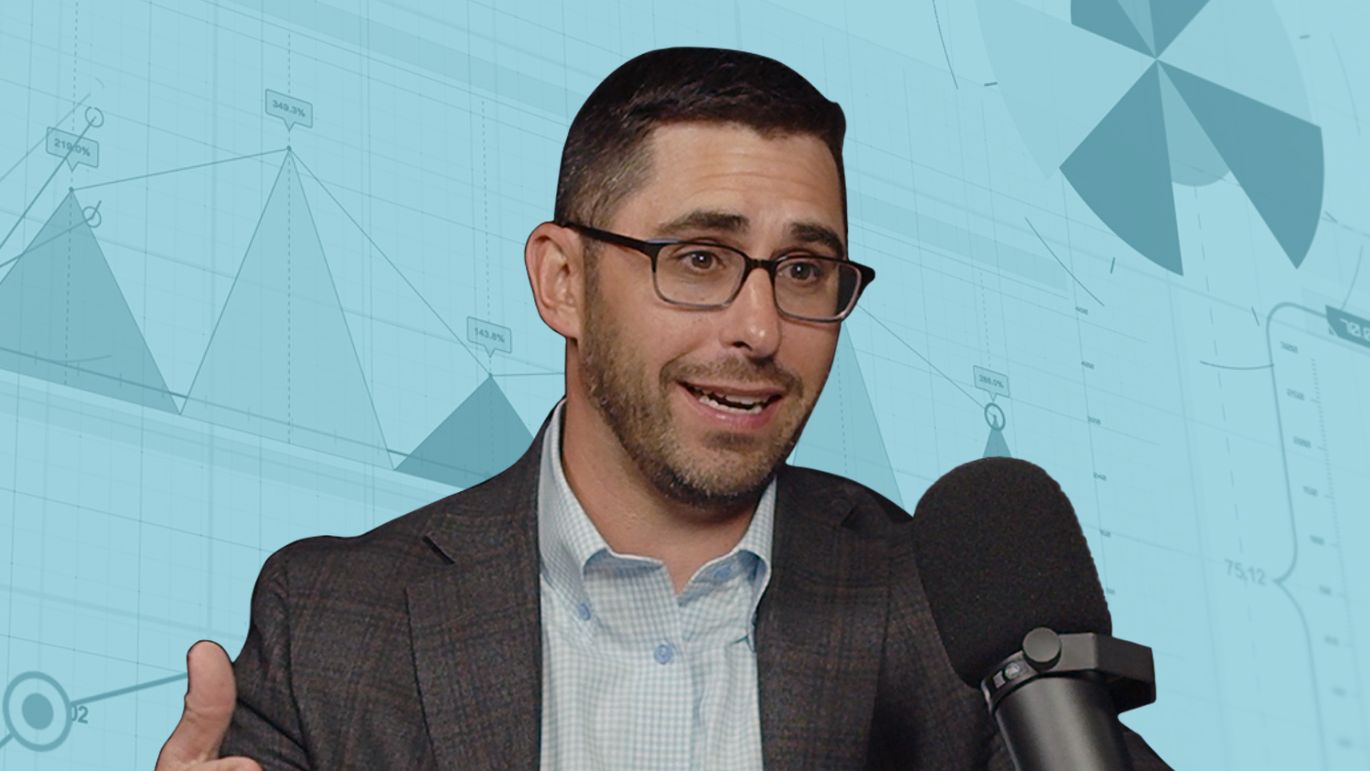 Person speaking into a microphone against a blue-toned background featuring business charts and graphs.