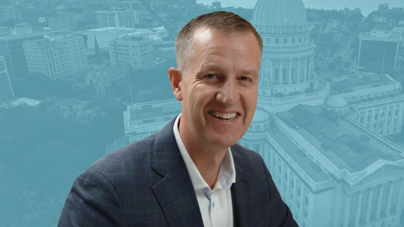Video thumbnail featuring a person in business attire, with an aerial view of the Wisconsin State Capitol and downtown Madison in the background.
