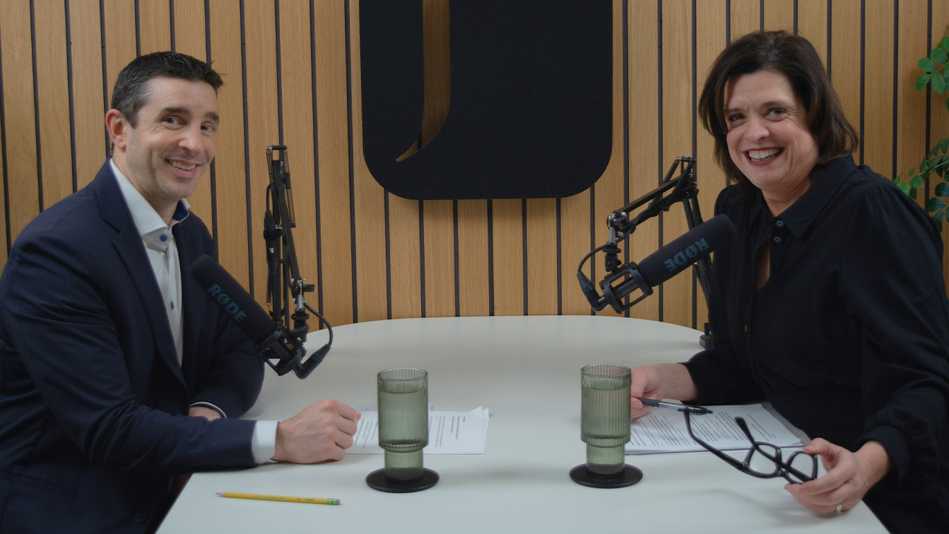 A smiling man and woman host a podcast or broadcast, seated at a table with professional microphones.