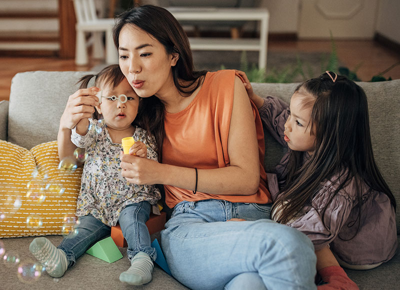 Mom blows soapy bubbles to entertain her two toddler daughters.