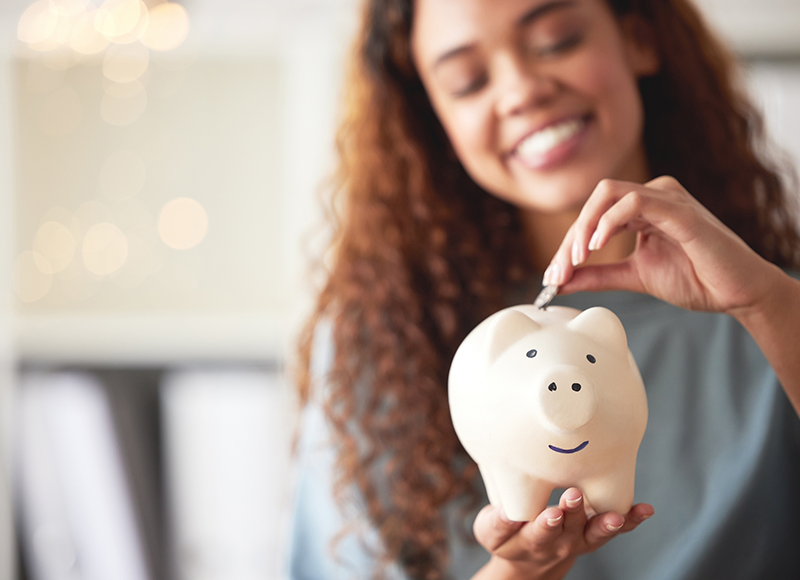 A woman is putting a coin into a piggy bank.