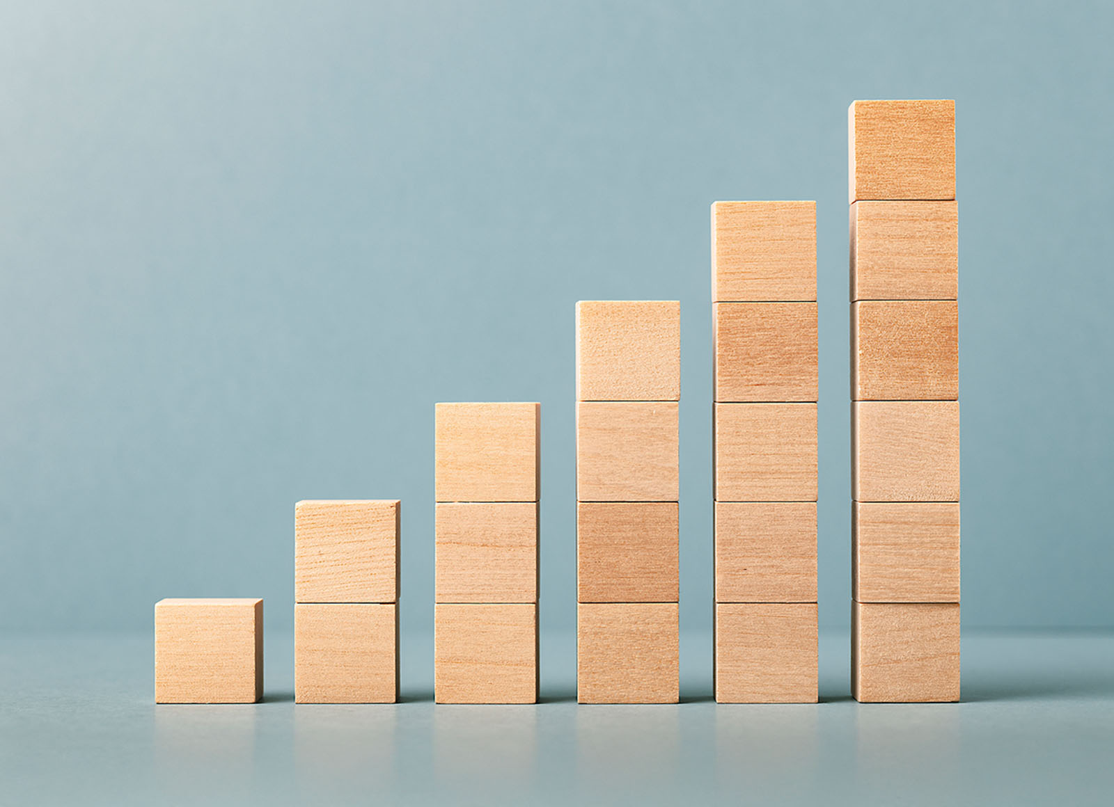 Stacked wooden blocks in ascending order, from shortest to tallest, symbolize gradual growth and progress.