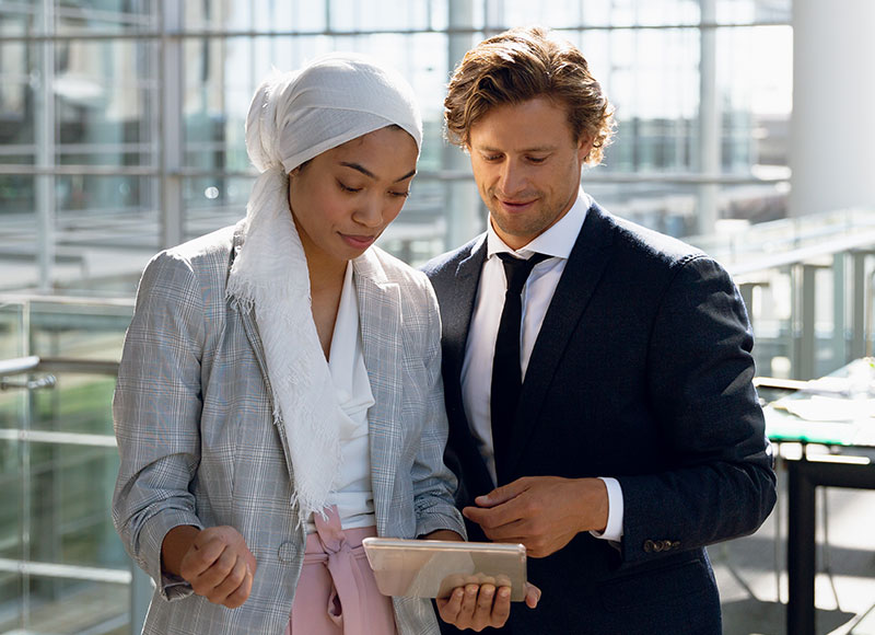 Coworkers stand together and review a document on a tablet screen.