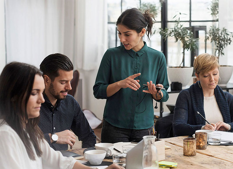 Manager giving instructions to colleagues during a meeting.