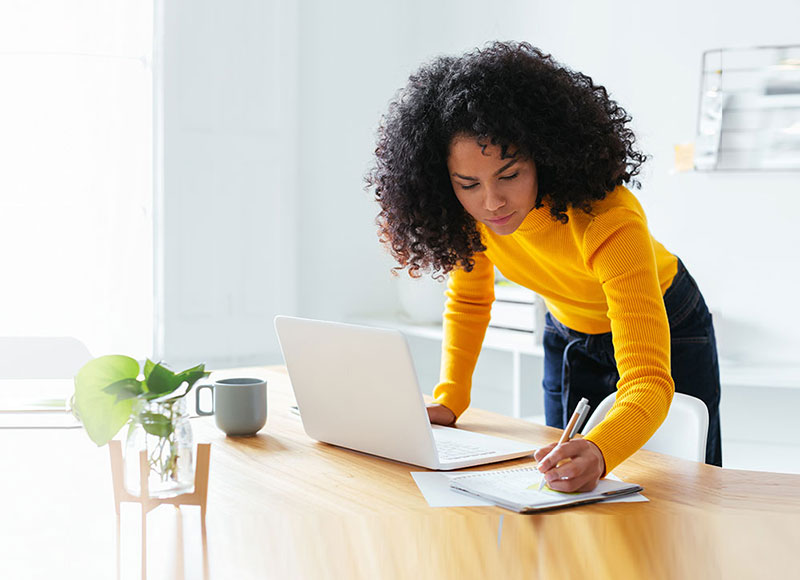 Woman in a yellow sweater works at a desk.