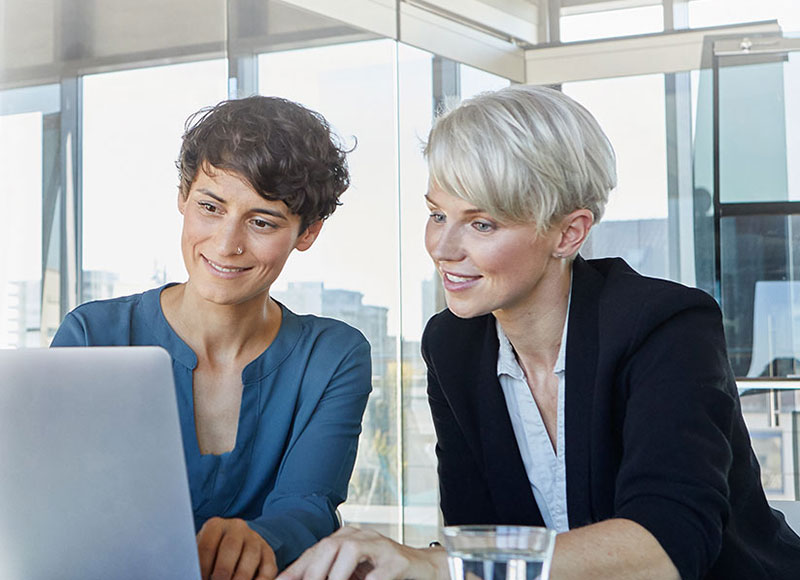 Female colleagues sit at a desk together and work on a laptop.