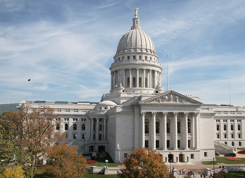 The image shows the Wisconsin State Capitol building, a white classical structure with a large dome and columns.