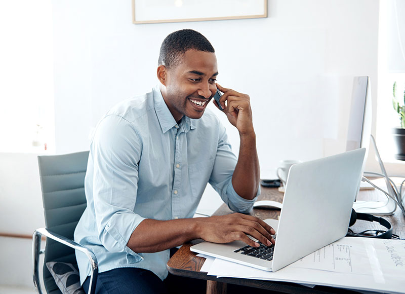 A man speaks to customer service over the phone while checking his computer.